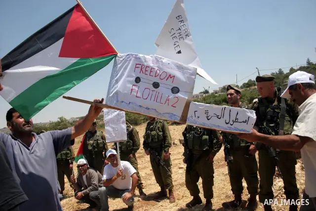 Israeli soldiers stand guard as Palestinian, Israeli and foreign activists hold a mock for the Gaza-bound international Freedom Flotilla during a demonstration against the demolishing of farm land to be used in the const...