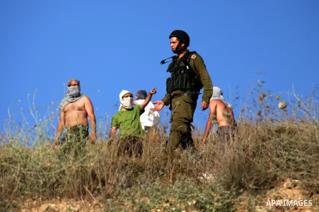 An Israeli soldier stands between masked Jewish settlers and Palestinians during clashes over farming land between the Jewish settlement of Yitzhar and the nearby West Bank village of Asira, near Nablus, Sunday, July 3,...