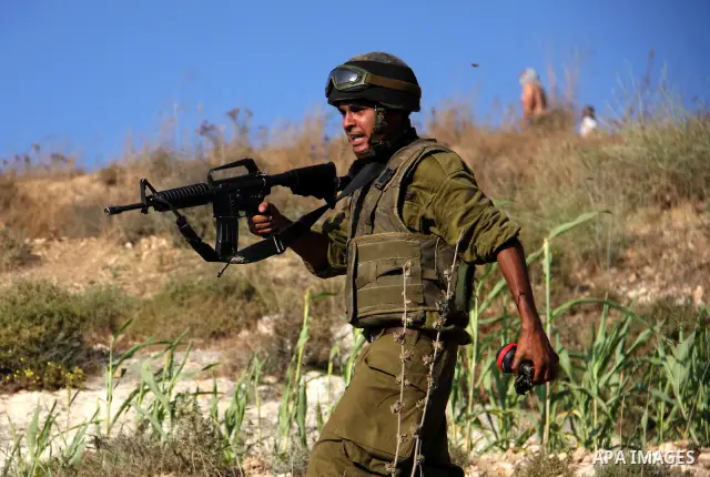 An Israeli soldier stands between masked Jewish settlers and Palestinians during clashes over farming land between the Jewish settlement of Yitzhar and the nearby West Bank village of Asira, near Nablus, Sunday, July 3,...