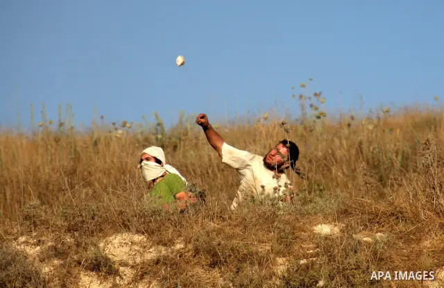 Masked Jewish settlers hurl stones towards Palestinian protesters, during clashes over farming land between the Jewish settlement of Yitzhar and the nearby West Bank village of Asira, near Nablus, Sunday, July 3, 2011. P...