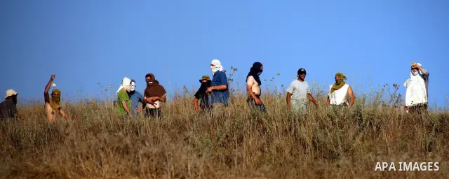 Masked Jewish settlers hurl stones towards Palestinian protesters, during clashes over farming land between the Jewish settlement of Yitzhar and the nearby West Bank village of Asira, near Nablus, Sunday, July 3, 2011. P...