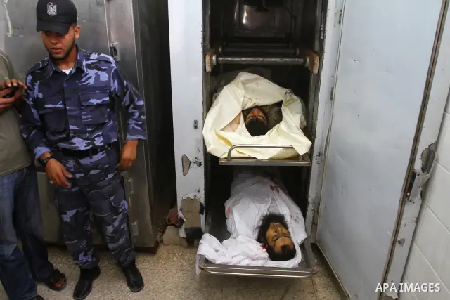 A Hamas security officer stands next to bodies of two Palestinians killed by Israeli forces, at the morgue of Al-Aqsa hospital in Deir Al Balah, central Gaza Strip, Tuesday, July 5, 2011. An Israeli attack struck a targe...