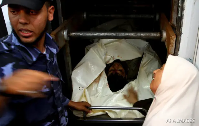 A woman and a Hamas security officer stand next to bodies of two Palestinians killed by Israeli forces, at the morgue of Al-Aqsa hospital in Deir Al Balah, central Gaza Strip, Tuesday, July 5, 2011. An Israeli attack str...