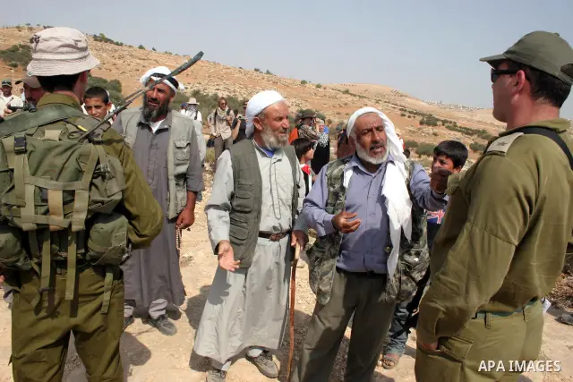 Palestinians argue with Israeli soldiers, as Israeli troops fire tear gas to disperse the protesters during a demonstration against the demolishing of farm land to be used in the construction of Jewish settlements near t...