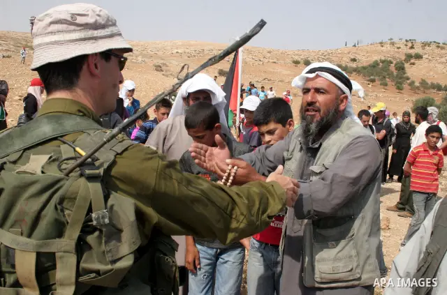 Palestinians argue with Israeli soldiers, as Israeli troops fire tear gas to disperse the protesters during a demonstration against the demolishing of farm land to be used in the construction of Jewish settlements near t...