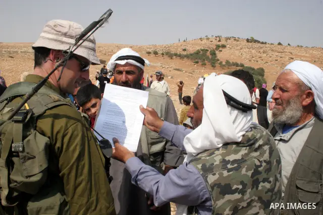 Palestinians argue with Israeli soldiers, as Israeli troops fire tear gas to disperse the protesters during a demonstration against the demolishing of farm land to be used in the construction of Jewish settlements near t...