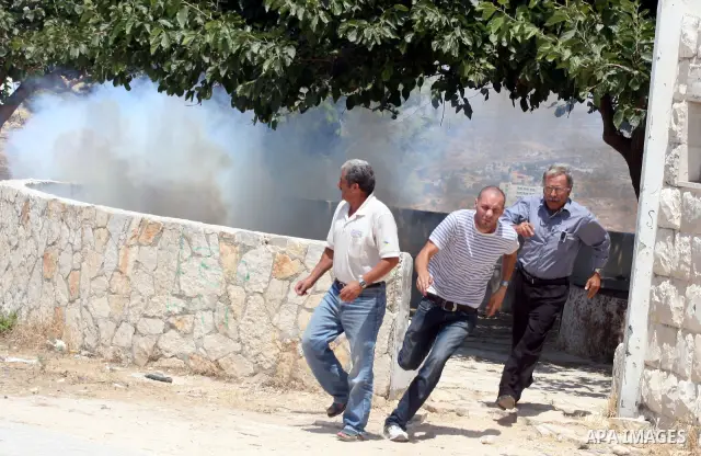 Palestinian protesters run for cover from tear gas canisters fired by Israeli soldiers in the West Bank village of Nabi Saleh, north of Ramallah, on July 22, 2011 during a weekly Friday protest against Israeli West Bank...