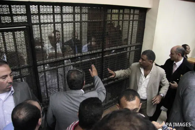 Journalists and bodyguards stand in the Cairo court room as defendants are kept behind bars, including Egypt's former Interior Minister Habib el-Adly, seen behind bars 3rd left, during their trial on charges relating to...