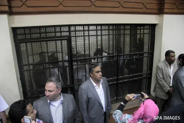 Journalists and bodyguards stand in the Cairo court room as defendants are kept behind bars, including Egypt's former Interior Minister Habib el-Adly, seen behind bars 3rd left, during their trial on charges relating to...