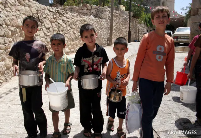 Palestinian families carry containers as they wait to receive free food for 'Iftar', the meal that breaks the daily fast during Ramadan, at an Islamic Council charity in the centre of the West Bank city of Hebron on Augu...