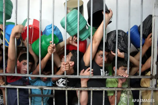Palestinian families carry containers as they wait to receive free food for 'Iftar', the meal that breaks the daily fast during Ramadan, at an Islamic Council charity in the centre of the West Bank city of Hebron on Augu...