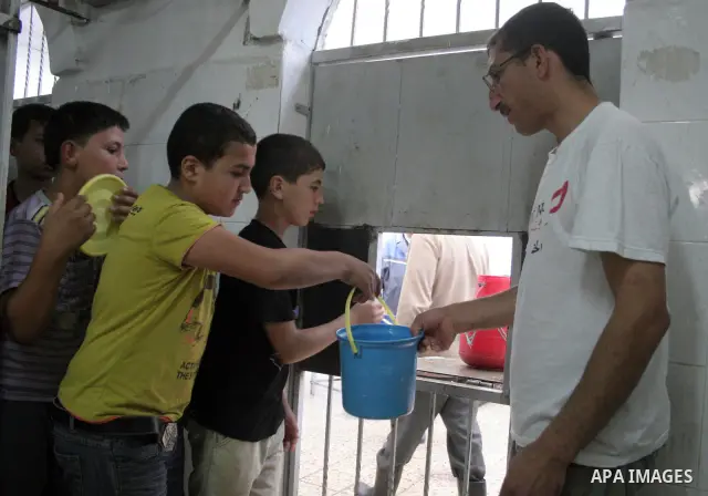 Palestinian families carry containers as they wait to receive free food for 'Iftar', the meal that breaks the daily fast during Ramadan, at an Islamic Council charity in the centre of the West Bank city of Hebron on Augu...