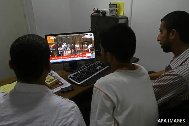 Palestinians watch the video image taken from Egyptian State Television shows 83-year-old Hosni Mubarak laying on a hospital bed inside a cage of mesh and iron bars as he flanked by his sons Alaa, left, and Gamal right,...