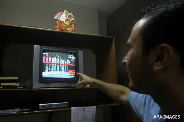 A Palestinian man watch the video image taken from Egyptian State Television shows 83-year-old Hosni Mubarak laying on a hospital bed inside a cage of mesh and iron bars as he flanked by his sons Alaa, left, and Gamal ri...