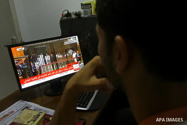 Palestinians watch the video image taken from Egyptian State Television shows 83-year-old Hosni Mubarak laying on a hospital bed inside a cage of mesh and iron bars as he flanked by his sons Alaa, left, and Gamal right,...