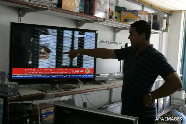 Palestinian men watch the video image taken from Egyptian State Television at a shop in Rafah, southern Gaza Strip, where shows 83-year-old Hosni Mubarak laying on a hospital bed inside a cage of mesh and iron bars as he...