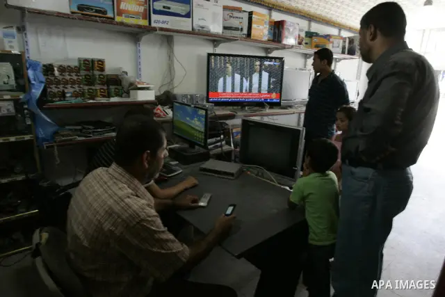Palestinian men watch the video image taken from Egyptian State Television at a shop in Rafah, southern Gaza Strip, where shows 83-year-old Hosni Mubarak laying on a hospital bed inside a cage of mesh and iron bars as he...