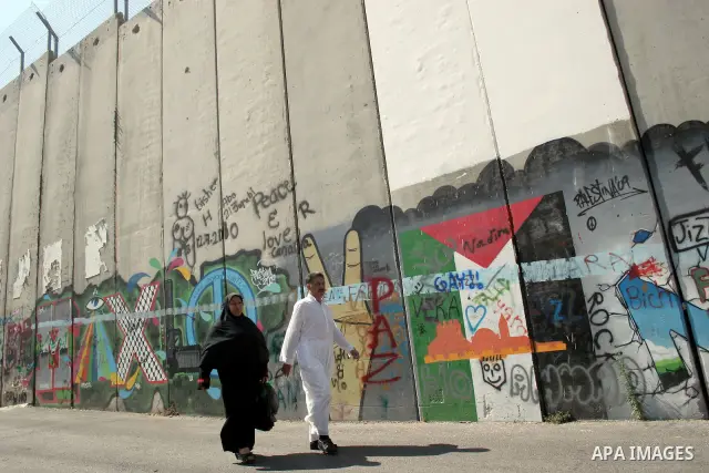 Palestinians walk past a mural painted on a section of the controversial Israeli barrier near an Israeli checkpoint to Jerusalem in the West Bank city of Bethlehem during the first Friday of the holy month of Ramadan Aug...
