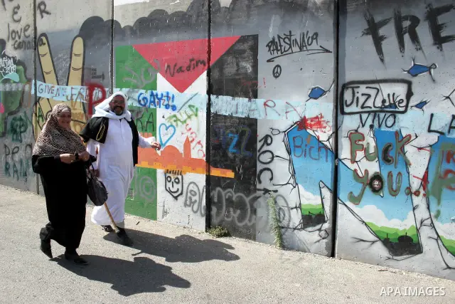 Palestinians walk past a mural painted on a section of the controversial Israeli barrier near an Israeli checkpoint to Jerusalem in the West Bank city of Bethlehem during the first Friday of the holy month of Ramadan Aug...