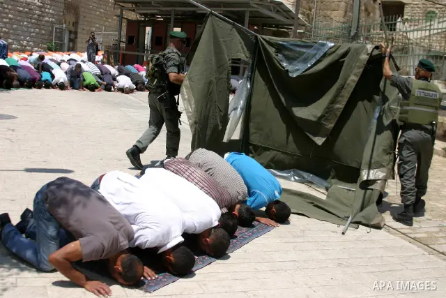 Israeli soldiers stand guard as Palestinian men perform the first Friday prayer of the holy Muslim month of Ramadan in front of the closed Ibrahimi mosque in the West Bank city of Hebron on Aug. 5, 2011. Photo by Najeh H...