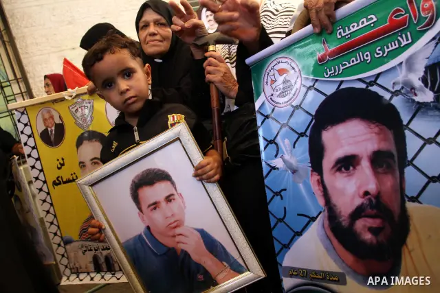 A Palestinian boy with his mother hold pictures of their prisoned relatives in Israeli jails as they gather in a weekly activity calling for their liberty at the Red Cross headquarters in Gaza City on Aug. 8, 2011. About...