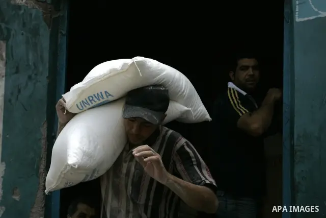 A Palestinian man carries a bag with wheat flour on his shoulders as others receive food aids from the United Nations Relief and Works Agency (UNRWA) at the Rafah refugee camp, in the southern Gaza Strip on August 15, 20...