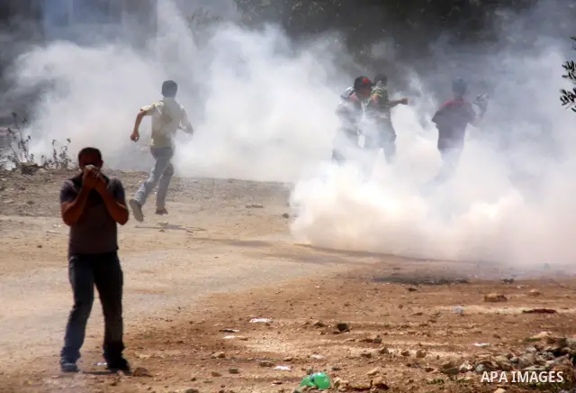 Palestinian demonstrators run as Israeli forces start to fire tear gas during clashes following a protest against the closure of a road during the second Intifada by Jewish settlers from the nearby settlement of Kadumim...