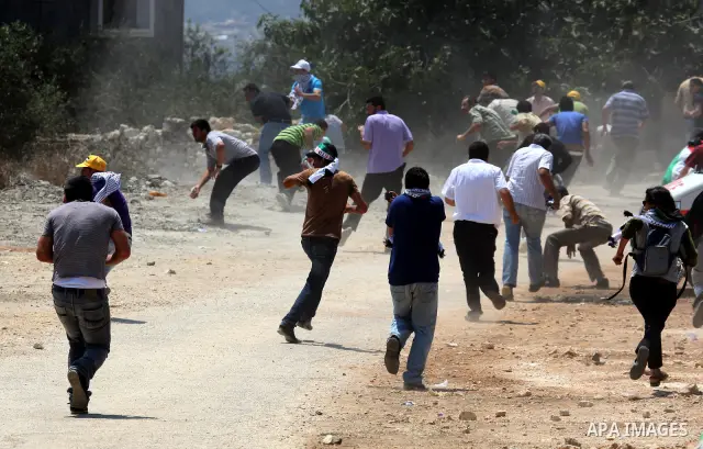 Palestinian demonstrators run as Israeli forces start to fire tear gas during clashes following a protest against the closure of a road during the second Intifada by Jewish settlers from the nearby settlement of Kadumim...