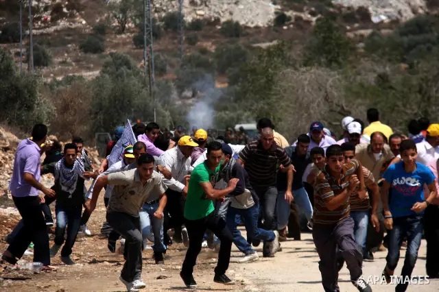 Palestinian demonstrators run as Israeli forces start to fire tear gas during clashes following a protest against the closure of a road during the second Intifada by Jewish settlers from the nearby settlement of Kadumim...