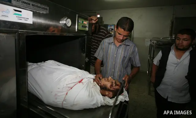 Palestinian men gather around the body of Mohammed Enaya at the mortuary of Al-Shifa hospital after he was killed when the Israeli air force targeted an area in the eastern part of Gaza City on August 19, 2011. Photo by...