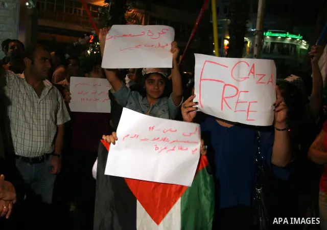 Palestinians wave with their national flag and hold placards during a protest in solidarity with the people in Gaza Strip, in the West Bank city of Ramallah on August 19,2011. Israel struck Gaza with two days of air stri...