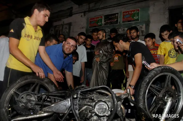 Palestinians inspect a destroyed motorcycle following an Israeli airstrike killing three Palestinian who were riding it, at the main road in Gaza City, Friday, Aug. 19, 2011. Palestinian official said that Dr. Monzer Qra...