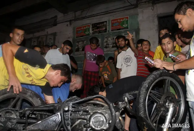 Palestinians inspect a destroyed motorcycle following an Israeli airstrike killing three Palestinian who were riding it, at the main road in Gaza City, Friday, Aug. 19, 2011. Palestinian official said that Dr. Monzer Qra...