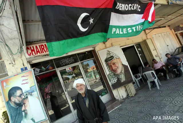 Palestinian people walk past a Libyan rebel flag in front of a shop in Gaza City, on August 24, 2011. The Hamas government and Palestinian liberation movements are reportedly showing solidarity with Libya after Libyan re...