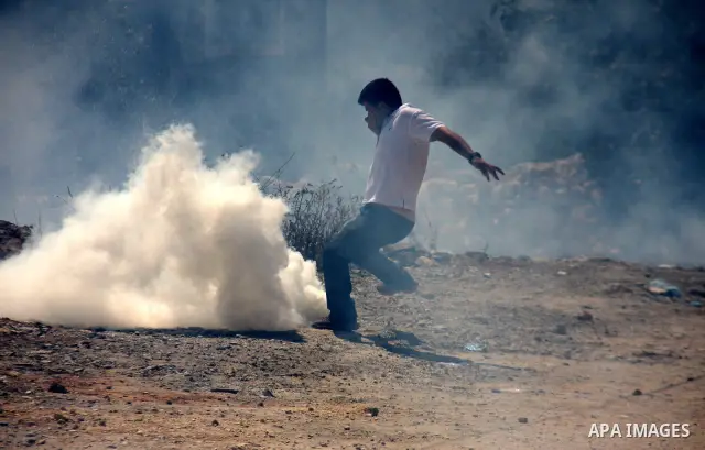 A Palestinian youth tries to seek cover from tear gas in clashes with Israeli troops during the weekly protest against the settlement of Qadomim, near the village of Kofr Qadom, west of Nablus City, in the Israeli-occupi...