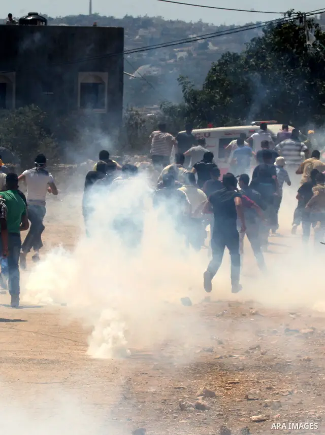 Palestinians run to seek cover from tear gas in clashes with Israeli troops during the weekly protest against the settlement of Qadomim, near the village of Kofr Qadom, west of Nablus City, in the Israeli-occupied West B...