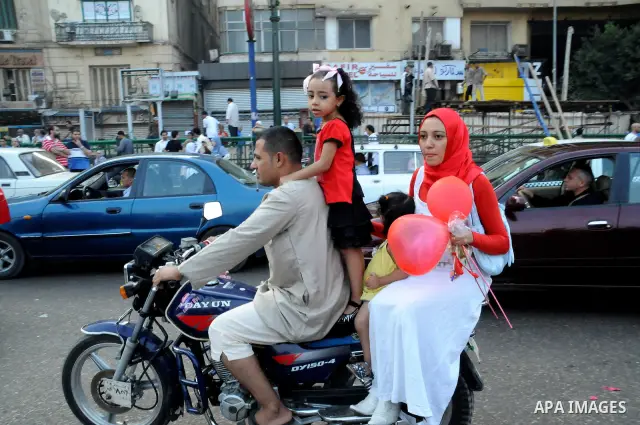 A man rides with his family a motorcycle as Egyptian Muslims gather to pray, celebrating the start of the three-day feast known in Arabic Eid al-Fitr, which marks the end of the holy fasting month of Ramadan, in Tahrir S...