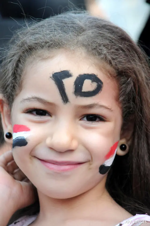 A girl paints her face with Egyptian flag as others gather to pray, celebrating the start of the three-day feast known in Arabic Eid al-Fitr, which marks the end of the holy fasting month of Ramadan, in Tahrir Square, th...