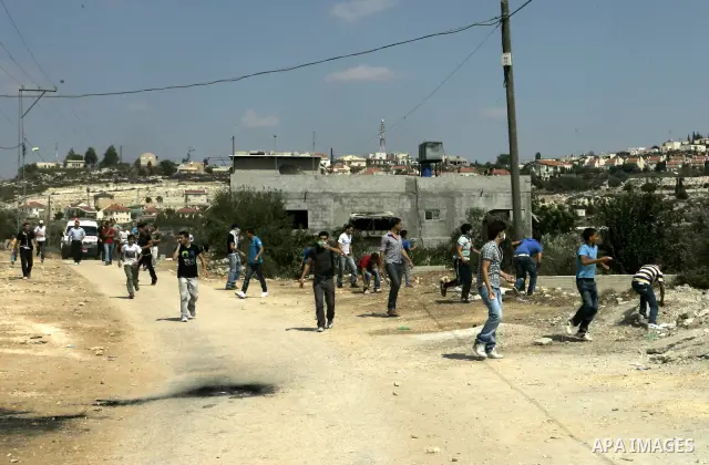 Palestinian demonstrators throw stones toward Israeli soldiers during a protest against the closure of a road during the second Intifada (uprising) by Jewish settlers from the nearby settlement of Kadumim (background), o...