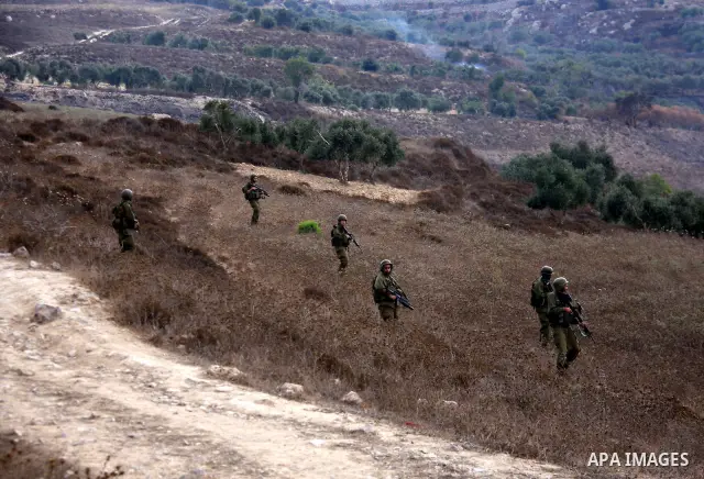 Israeli soldiers patrol in a field as villagers try to extinguish fires in a olive grove and fields which according to the local Palestinian villagers was started by settlers from a near by Jewish settlement close to the...