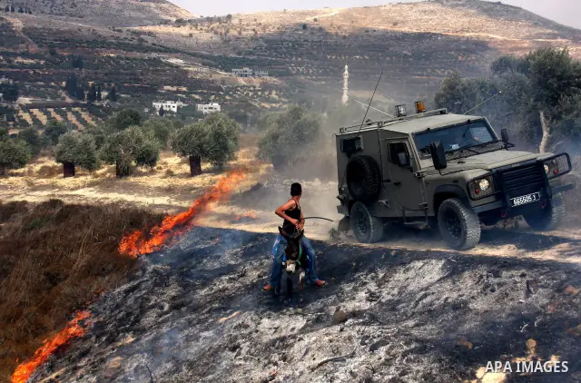 A Palestinian man rides a donkey past an Israeli military jeep as villagers try to extinguish fires in a olive grove and fields which according to the local Palestinian villagers was started by settlers from a near by Je...