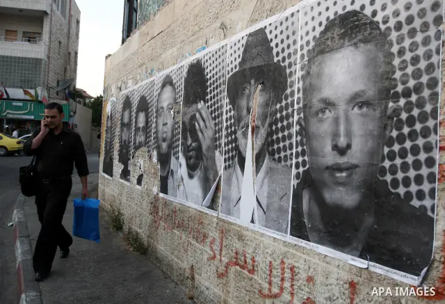 A Palestinian man walks past large black and white photographs taken by French street artist JR of Palestinians, on September 6, 2011, in the West Bank city of Ramallah. JR's project entails having Palestinian and Israel...