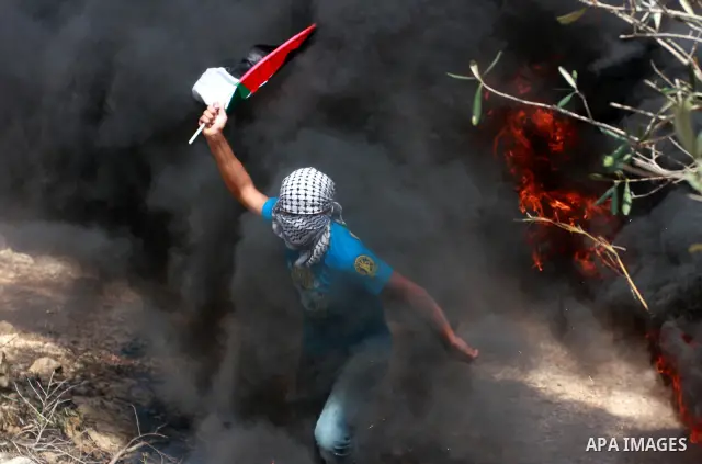 Masked Palestinian waves Palestine National flag as he run to seek cover from smokes, during the weekly protest against the settlement of Qadomim, near the village of Kofr Qadom, west of Nablus City, in the Israeli-occup...