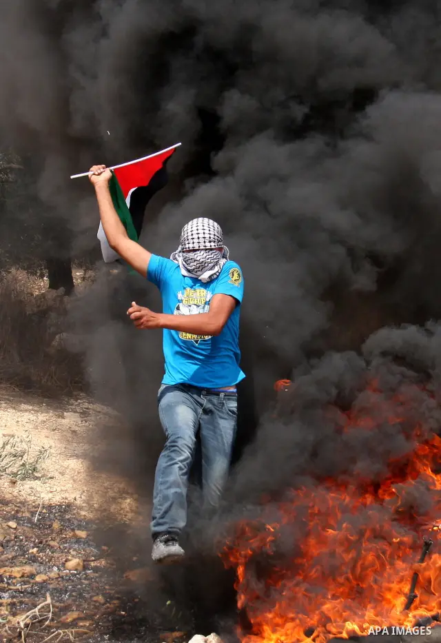 Masked Palestinian waves Palestine National flag as he run to seek cover from smokes, during the weekly protest against the settlement of Qadomim, near the village of Kofr Qadom, west of Nablus City, in the Israeli-occup...