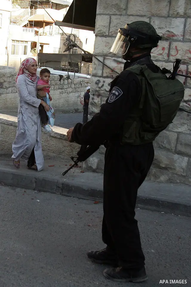 A Palestinian woman walks past Israeli riot policeman standing guard in the east Jerusalem neighborhood of Silwan on Sep. 13, 2011 following brief clashes between police and Palestinian stone throwers. Photo by Mahfouz A...