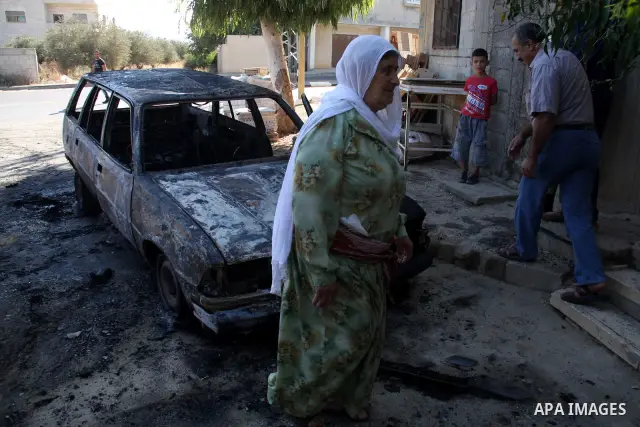 A Palestinian woman walks next to a burnt car in the village of Beit Furik, near the West Bank town of Nablus, on Sept. 15, 2011. Vandals set fire to three cars in a West Bank village, and suspicion has fallen on Jewish...