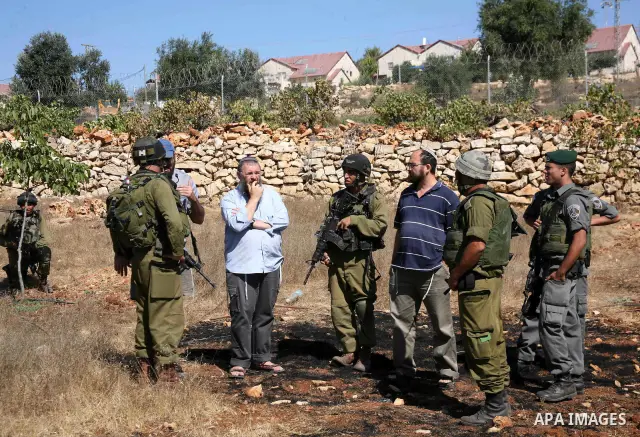 Israeli soldiers and settlers from the Jewish settlement of Karmei Tzur stand by as Palestinian and international activists (not pictured) work on a Palestinian's farm land in the West Bank village of Beit Omar near Hebr...