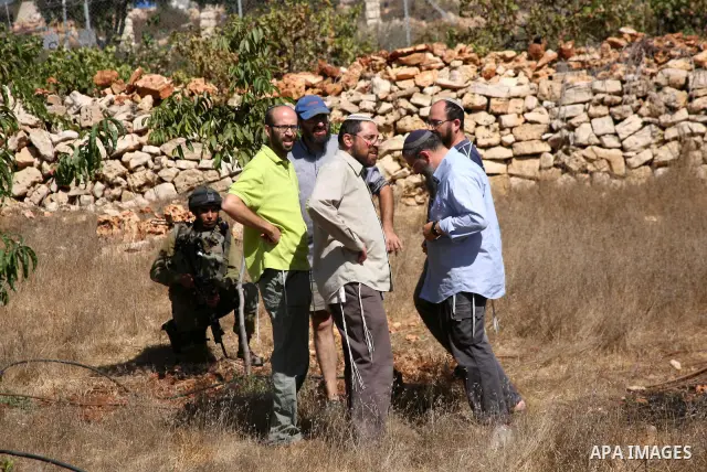 Israeli soldiers and settlers from the Jewish settlement of Karmei Tzur stand by as Palestinian and international activists (not pictured) work on a Palestinian's farm land in the West Bank village of Beit Omar near Hebr...