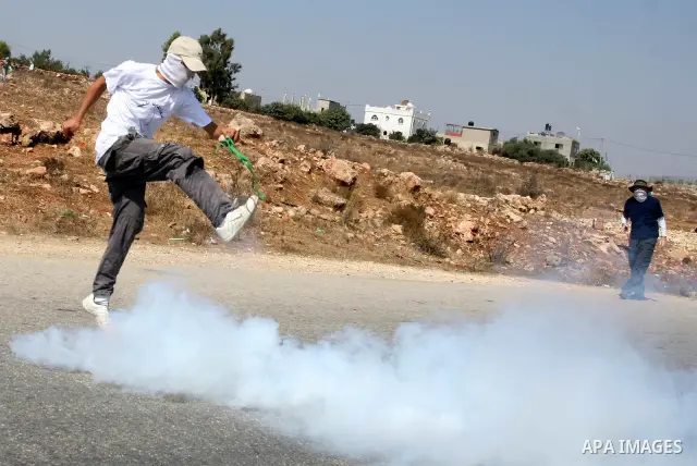 A Palestinian demonstrator kicks a tear gas canister fired by Israeli soldiers during a protest against the expansion of the nearby Jewish settlement of Halamish, in the West Bank village of Nabi Saleh, near Ramallah, Fr...