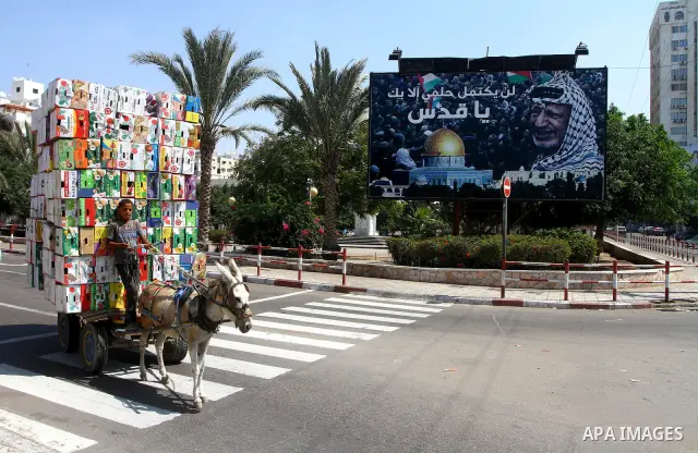 A Palestinian boy rides his donkey cart past a billboard which bears a portait of late Palestinian leader Yasser Arafat, with the Arabic slogan: "My dream will not be compete without Jerusalem," in central Gaza City on S...